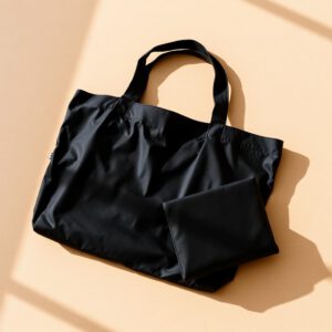 Black fold-flat tote bag beside its folded storage pouch